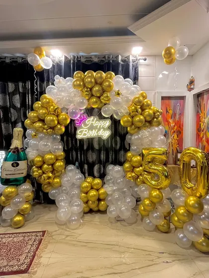 The final 50th birthday decoration, featuring a stunning gold and white balloon arch, a champagne bottle prop, and large '50' foil numbers.