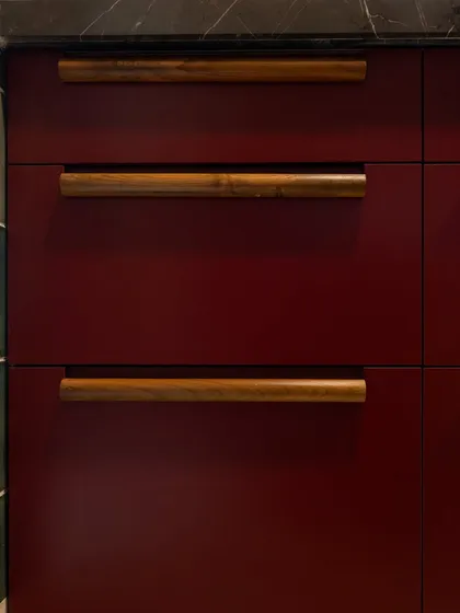 A detailed shot of the custom wooden handles on the Marsala red drawers. The natural grain and simple form of the wood provide a beautiful, tactile contrast to the smooth, lacquered finish of the cabinets.