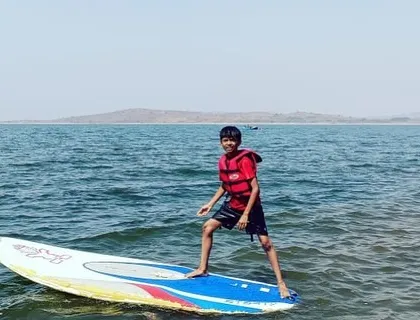A young boy confidently stands on his paddleboard, enjoying the vast open water of Vani Vilas Sagar.