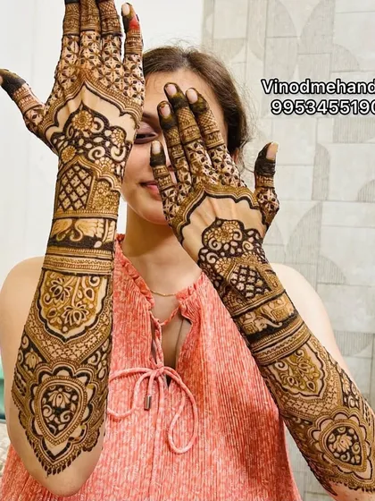 A happy bride showing off her full-arm mehandi. This design features architectural domes and classic Indian motifs, creating a symmetrical and balanced look across both arms.