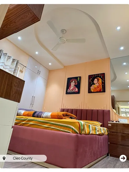 A bedroom filled with color and personality. The deep pink velvet bed contrasts beautifully with the peach walls and the client's own artwork, creating a vibrant, artistic retreat.
