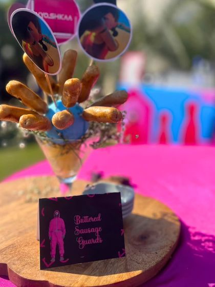 A creative presentation of 'Buttered Sausage Guards' for the 'Squid Game' party. The custom food label clearly communicates the themed dish, adding to the fun and immersive experience for guests.