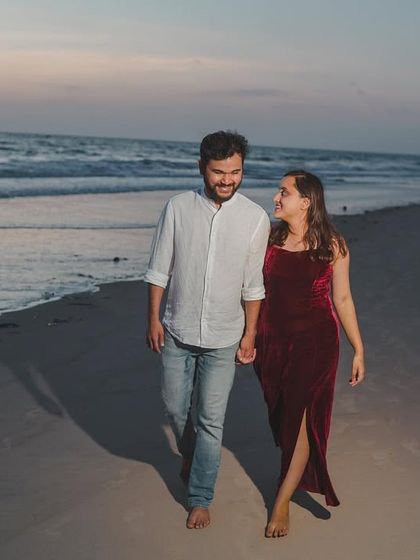 A candid moment of the couple walking and talking on the sand, with the beautiful evening light creating a soft, romantic atmosphere.
