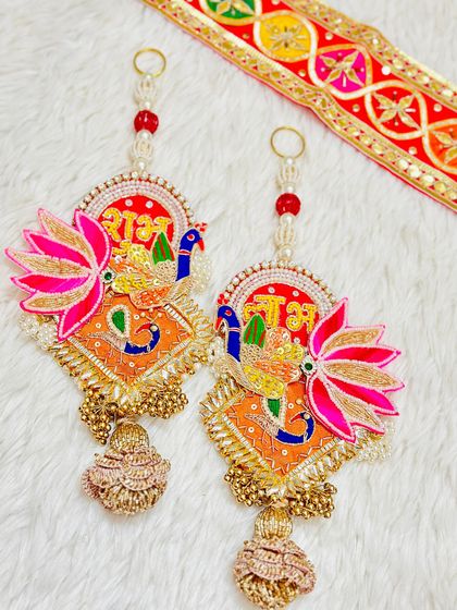 A beautiful Shubh Labh hanging with Ganesha and peacock motifs. The combination of orange and pink, along with delicate beadwork, makes this a standout piece.