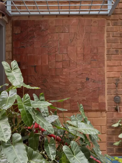 A subtle relief carving on a wall of reddish stone blocks. The artwork is integrated so seamlessly with the building material that it appears to emerge from the wall itself.
