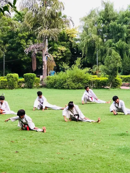 Students holding a seated forward bend during an outdoor class. This pose builds hamstring flexibility and teaches the discipline of holding through discomfort.
