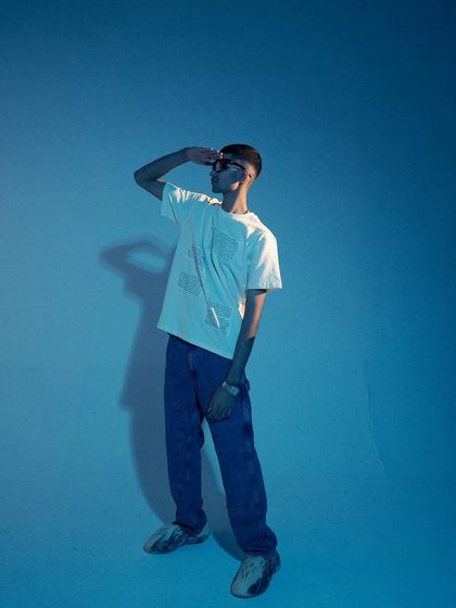 A composed, standing pose with a strong shadow. The use of a single light source creates a dramatic and minimalist look, perfect for a modern streetwear brand.