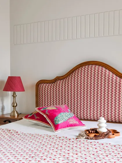 This guest bedroom in 'Project Lily' features a vibrant pink and red color scheme with a custom-upholstered headboard and intricate wall molding.