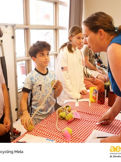 A sixth-grader explains his upcycled product to a teacher at the mela. This project-based learning experience combines social studies, design, and entrepreneurship.