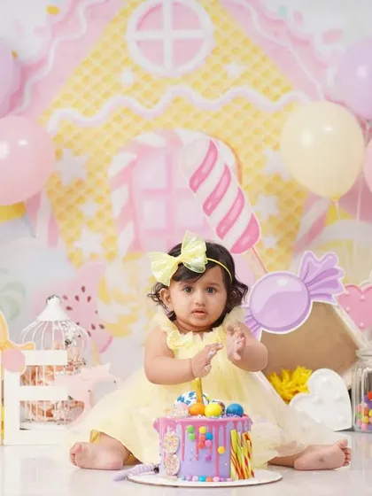 A baby girl sits in front of her birthday cake in a vibrant Candyland-themed set, complete with giant candy props and pastel balloons.