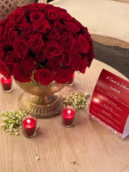 A close-up of the personalized table menu for "A Toast to Jahan," set amongst beautiful red roses and candles. The menu design and decor worked together to create a cohesive and romantic theme.