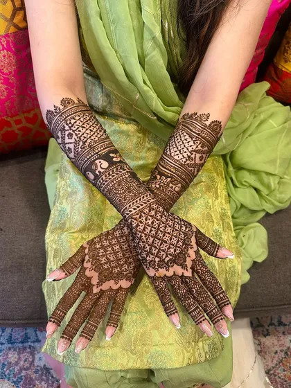 A classic jaali net pattern covers the hands, accented with bold cuff designs on the wrist and forearm for a sophisticated and traditional mehndi look.