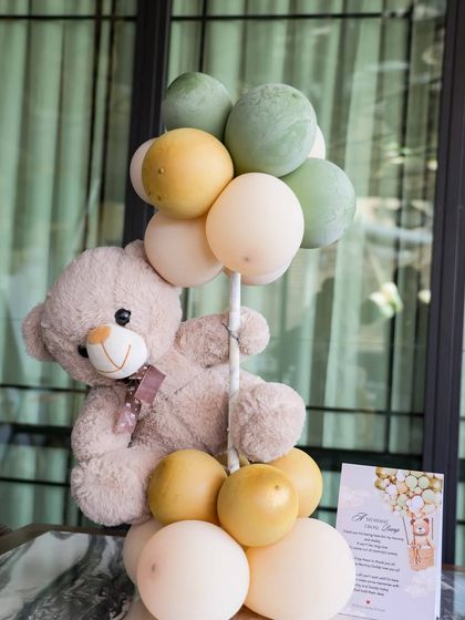 An adorable teddy bear centerpiece, holding onto a bouquet of balloons. This simple yet effective decoration adds a touch of whimsy to each guest table.