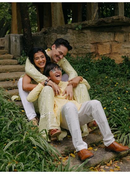 A playful and joyous moment from a Haldi ceremony. The couple shares a laugh with a young family member, creating a heartwarming and authentic family portrait.