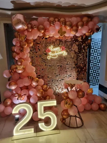 A different angle of the rose gold 25th-anniversary setup, showcasing the shimmer wall and the extensive balloon garland.