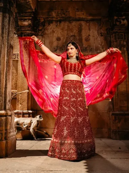 A portrait of the bride in a stunning red lehenga, framed by the pillars of a stepwell. The light catches her flowing dupatta, creating a beautiful, regal image.