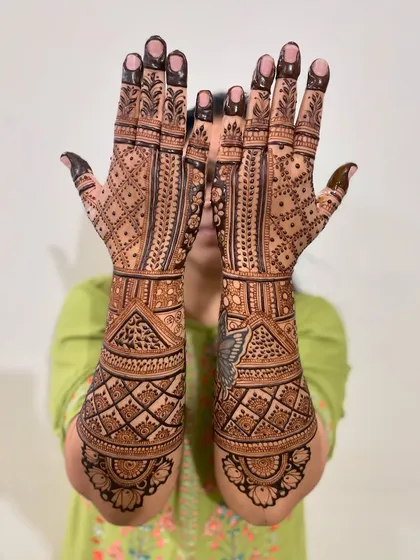 A happy bride showing off her geometric-style bridal mehendi. The design covers her hands and arms completely for a rich, traditional look.