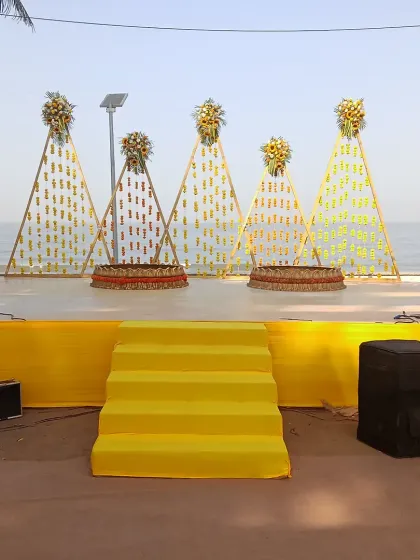 This Haldi stage was designed for a beach event, using bright yellow fabric and creative backdrops made of marigold strings in a triangular pattern. It's a modern take on traditional decor.