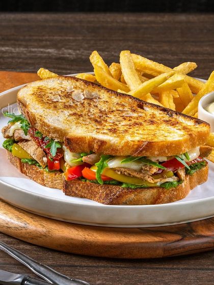 A grilled chicken and pepper sandwich, packed with colorful ingredients and served with a side of fries.