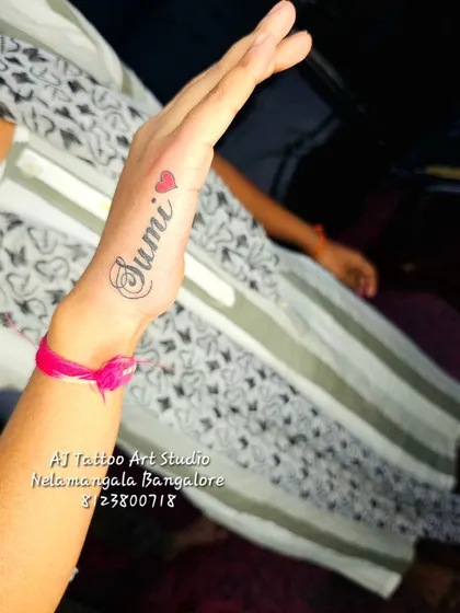 A "Sumi" name tattoo with a small heart on the side of the hand.