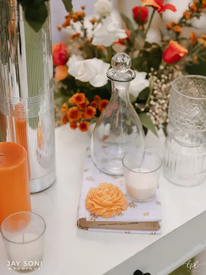 A close-up of a console table detail, featuring an orange flower carved from soap, a glass decanter, and candles, showing the thought put into every small element.
