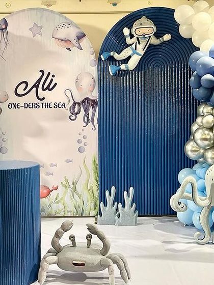 Ali's 'One-ders the Sea' birthday party featured a cool blue color palette. The decor included an astronaut exploring the ocean, cute octopus and crab props, and a light-up number '1'.