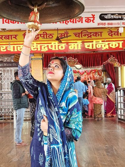 Ringing the temple bell, this image captures a moment of devotion. The traditional blue printed suit is perfect for such a sacred occasion.