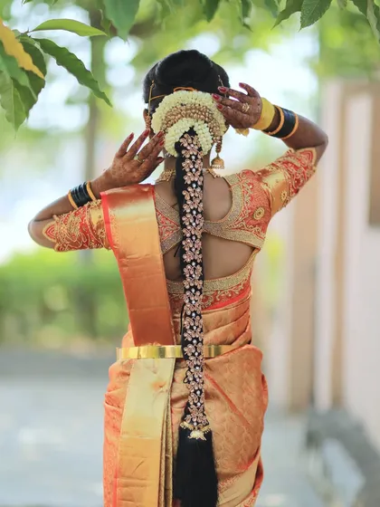 A South Indian bridal look is incomplete without a traditional hairstyle. This classic long braid is adorned with fresh jasmine flowers and a beautiful hair accessory, perfectly complementing the bride's muhurtham saree and temple jewellery.