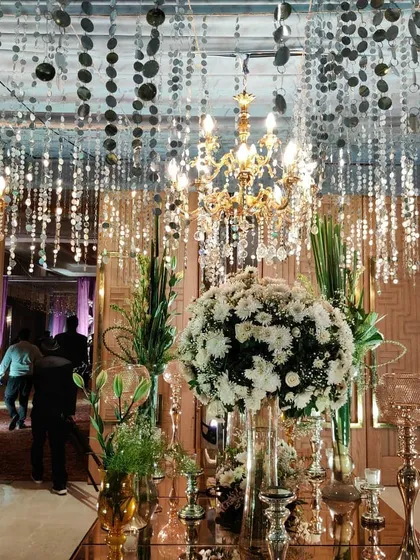 A detail shot of the sangeet decor, showing the shimmering ceiling installation, crystal chandeliers, and large bouquets of white chrysanthemums.