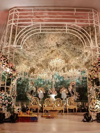 A modern, structural mandap with a canopy of dense, rustic foliage and dozens of hanging crystal chandeliers. The design blends natural textures with glamorous elements for a unique and romantic effect.