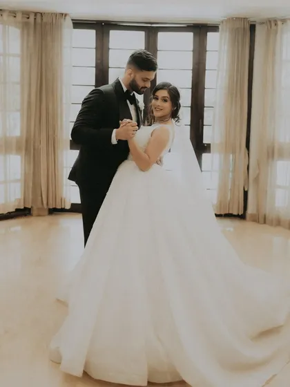A classic portrait of the couple sharing their first dance in a beautifully lit room, the bride's ball gown in full view.