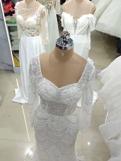 For the bride who loves glamour, this fully beaded white gown is a showstopper. The long sleeves and square neckline are covered in intricate pearl and sequin work, creating a look of pure opulence.
