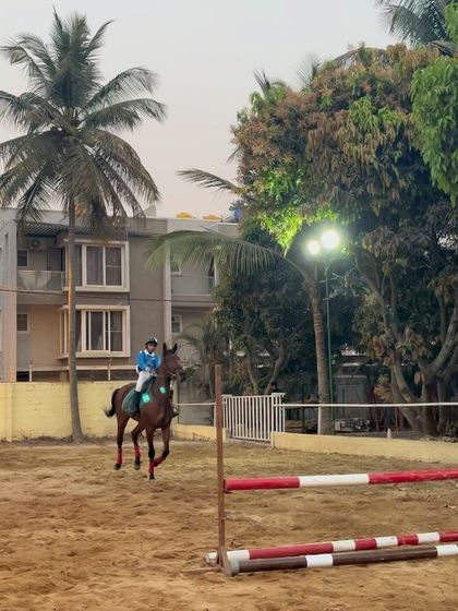 A rider maintains focus and form while navigating a jumping course during a training camp. The well-lit arena allows for productive practice sessions even after sunset.