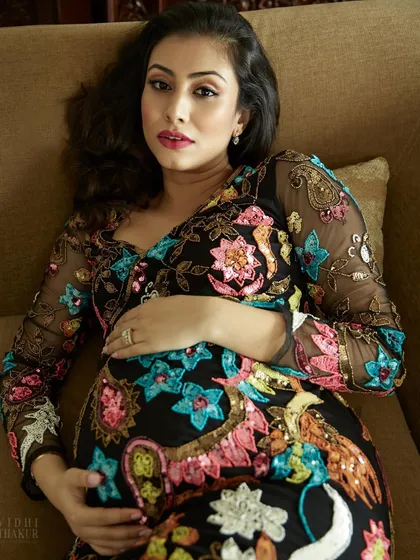 A powerful and artistic maternity portrait captured during an in-home session. The vibrant embroidery of her dress and the direct gaze create a striking image that celebrates the vitality and strength of pregnancy.
