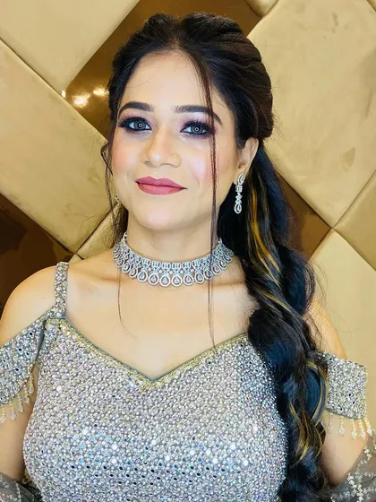 A beautiful party makeup look on a client in a silver sequined outfit. Her hair is styled in a voluminous side braid, and her makeup features a soft smokey eye.