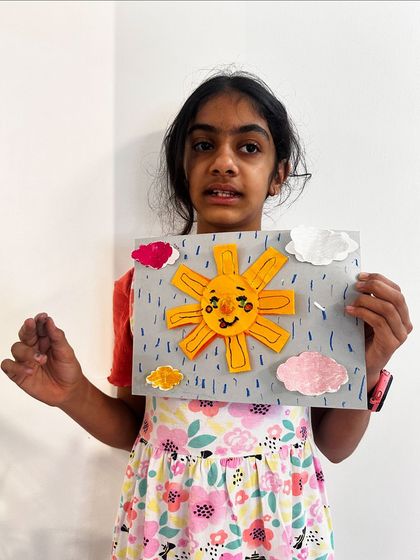 A student from our sun craft class shows off her cheerful creation, complete with a happy face and fluffy clouds.
