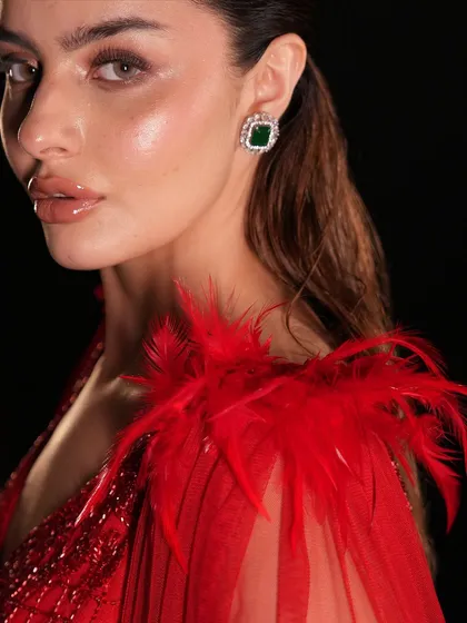 A close-up on the craftsmanship of the red gown. The vibrant red feathers on the shoulder add a touch of couture elegance to this stunning cocktail outfit.