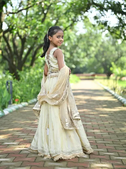 A back view of the custom ivory kids' lehenga, showing the delicate lace-up detail on the back of the blouse and the flowing dupatta.