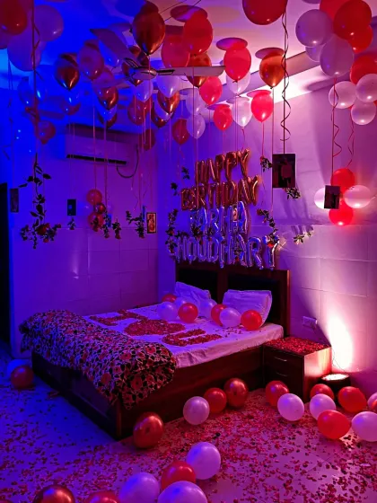 For this birthday surprise, I used moody blue and purple lighting to create a vibrant, celebratory atmosphere. The room is filled with red and white balloons on the ceiling and floor, with 'Happy Birthday' foil balloons and photos of the couple hanging above the bed.