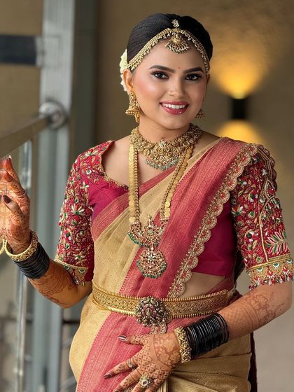 A happy bride in a beautiful red and gold Kanjeevaram. Her makeup is bright and glowing, with a classic hairstyle adorned with flowers.