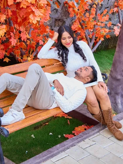 A relaxed and intimate moment on a park bench, surrounded by beautiful autumn-colored foliage, showcasing a cozy and natural pre-wedding theme.
