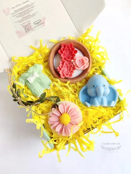 A look inside one of my curated gift hampers, created for a baby shower. This box features a succulent-themed clay pot candle, a baby elephant candle, a daisy wax sachet, and a baby onesie fridge magnet, all nestled in bright yellow shred. It shows how I can combine different handmade products into one beautiful, cohesive gift.