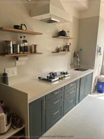 This kitchen perfectly balances color and natural texture. The leafy green European membrane-finished shutters are paired with open wooden shelves, creating a functional space that feels both organized and inspired by nature.
