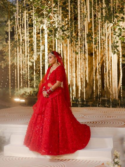 Aashna standing against a magical backdrop. Her classic red bridal makeup stands out beautifully, creating a truly cinematic wedding portrait.