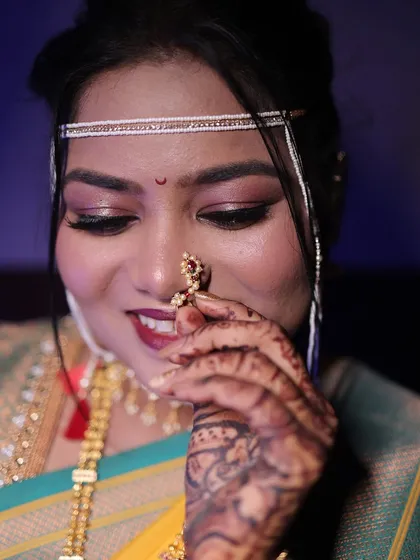 A close-up of the bride adjusting her nath, a classic pose. The focus is on her beautiful eyes and the traditional jewellery.