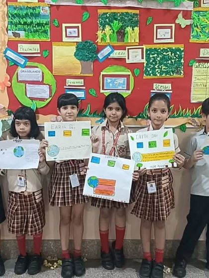 Students stand in front of a bulletin board decorated with grasslands-themed art, holding up their Earth Day posters. Our classroom environments are designed to be immersive and inspiring.