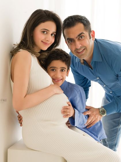 A beautiful family portrait celebrating their growing family. The son hugs his mother's baby bump, a sweet moment of connection before the new arrival.