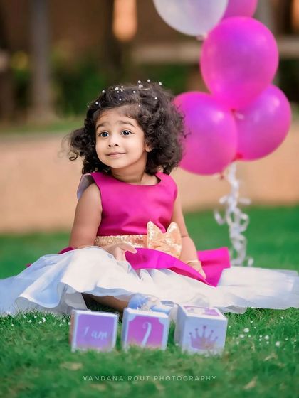 Celebrating two years with a lovely outdoor birthday shoot. The pink balloons and 'I am 2' blocks add a festive touch to this adorable toddler portrait.