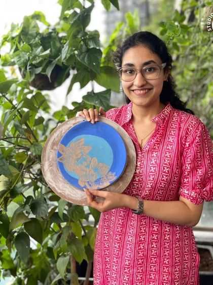 A student proudly displays her beautiful blue Sgraffito plate with a delicate floral design, created in our workshop.