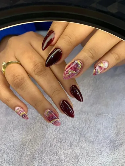 A beautiful set of almond-shaped nails in a deep wine color, with accent nails featuring a pink and gold marble effect.